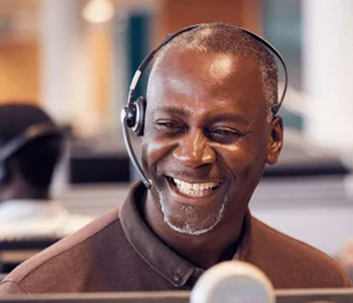 Smiling man wearing a headset sits in front of a computer Smiling man wearing a headset sits in front of a computer