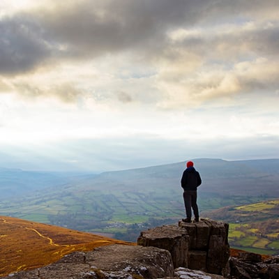 A man standing on a tree stump looking out at the landscape and clouds before him A man standing on a tree stump looking out at the landscape and clouds before him