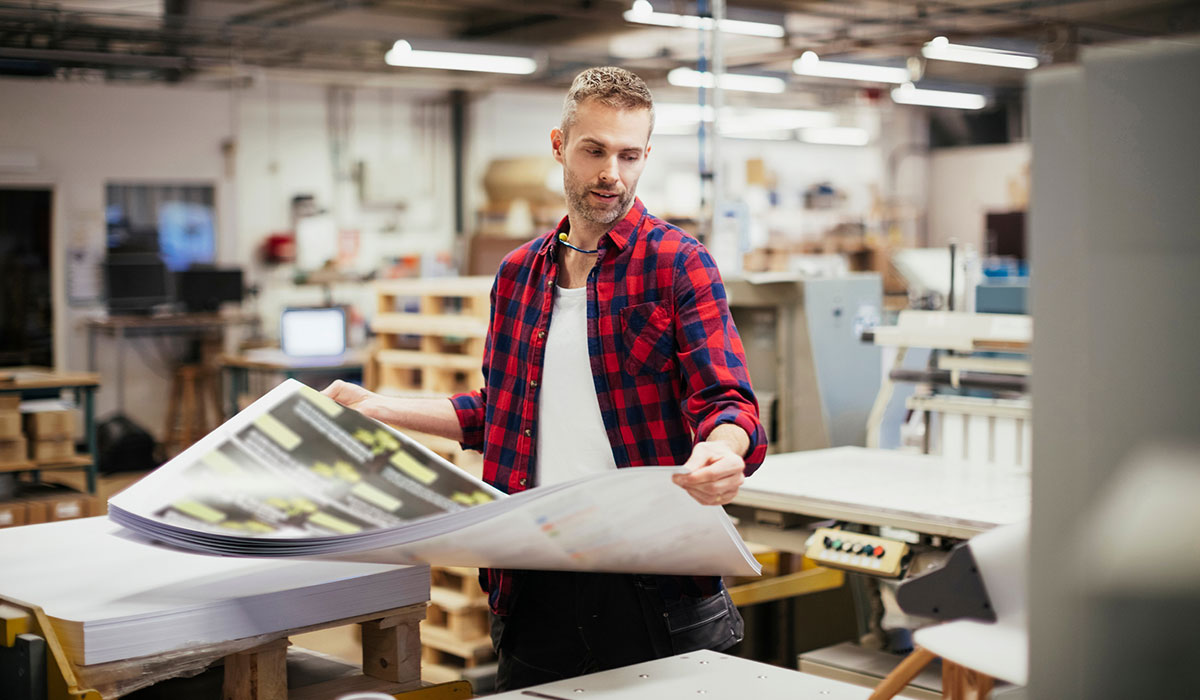 Person holding pile of printed papers in a print factory Person holding pile of printed papers in a print factory