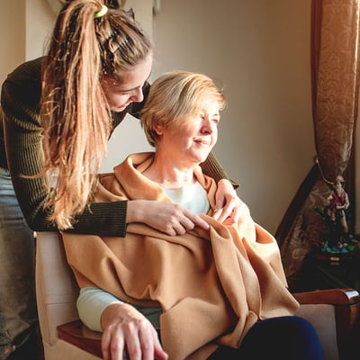 A social worker wrapping a blanket around an older woman in a chair A social worker wrapping a blanket around an older woman in a chair