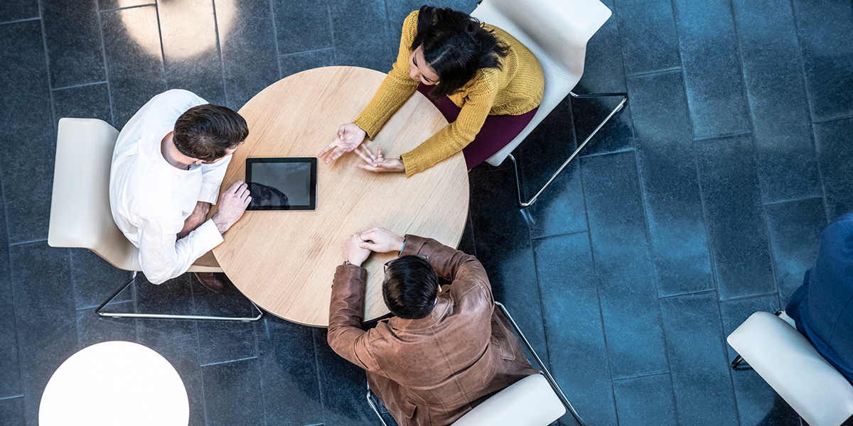 Birds-eye view of a group sat working remotely at a table. Birds-eye view of a group sat working remotely at a table.