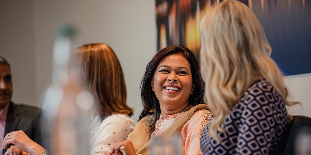 Two women talking and laughing together at a conference table. Two women talking and laughing together at a conference table.