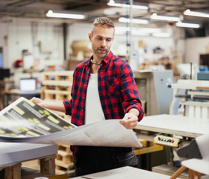 Man in a print manufacturing facility looking at a pile of printed material Man in a print manufacturing facility looking at a pile of printed material